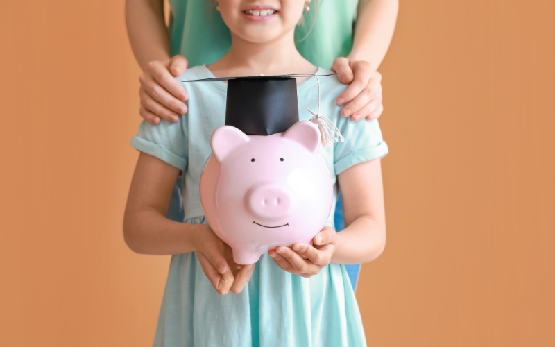 Child holding piggy bank with grad cap and adult behind them